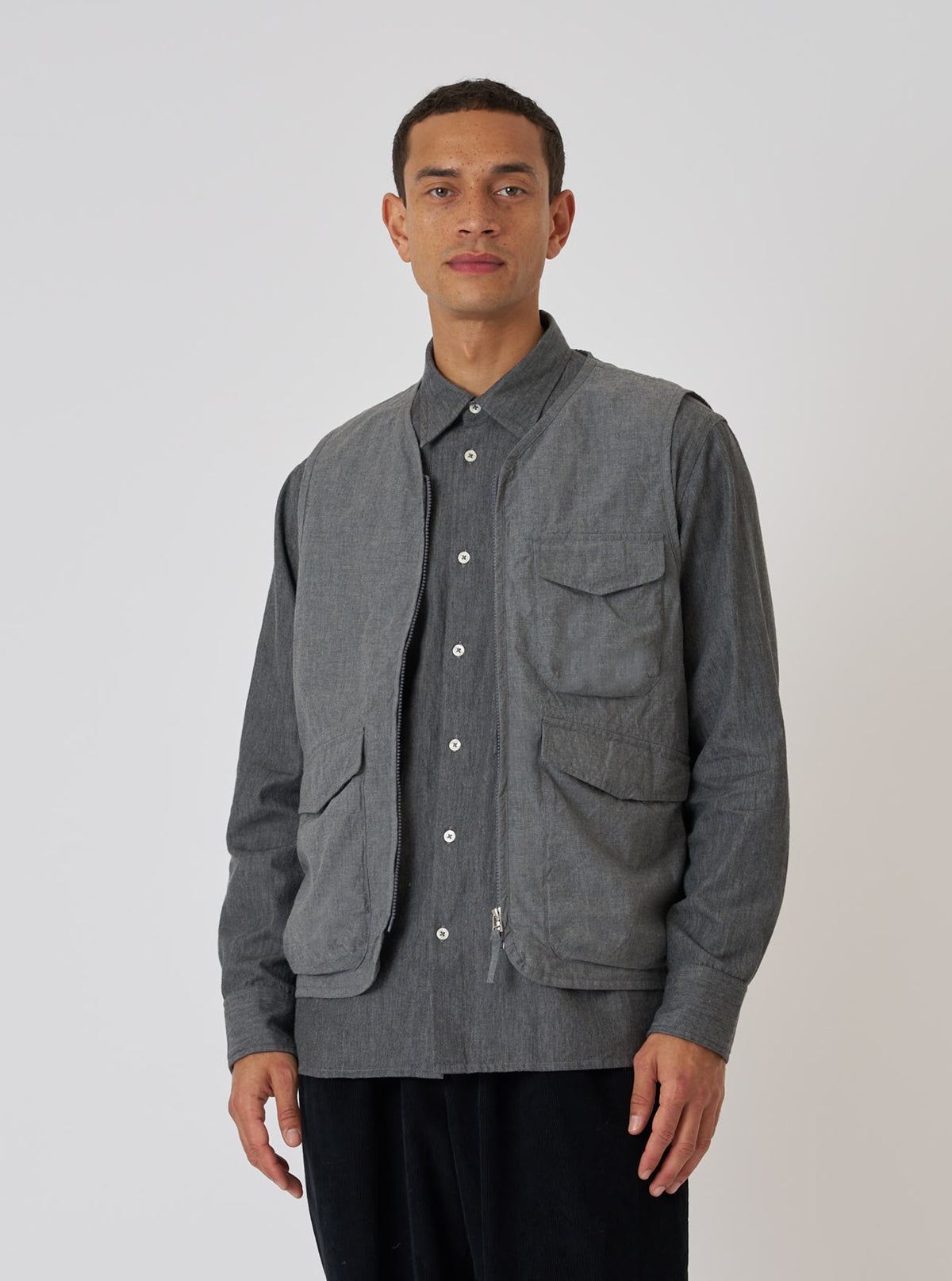 A model poses in front of a white background wearing a Charcoal Organic Chambray Parachute Liner Gilet. The gilet is charcoal gray and made of chambray material.