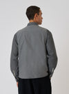 Back view of a model wearing a Charcoal Organic Chambray Parachute Liner Gilet over a long-sleeved shirt. The gilet is a charcoal color and made of organic chambray.