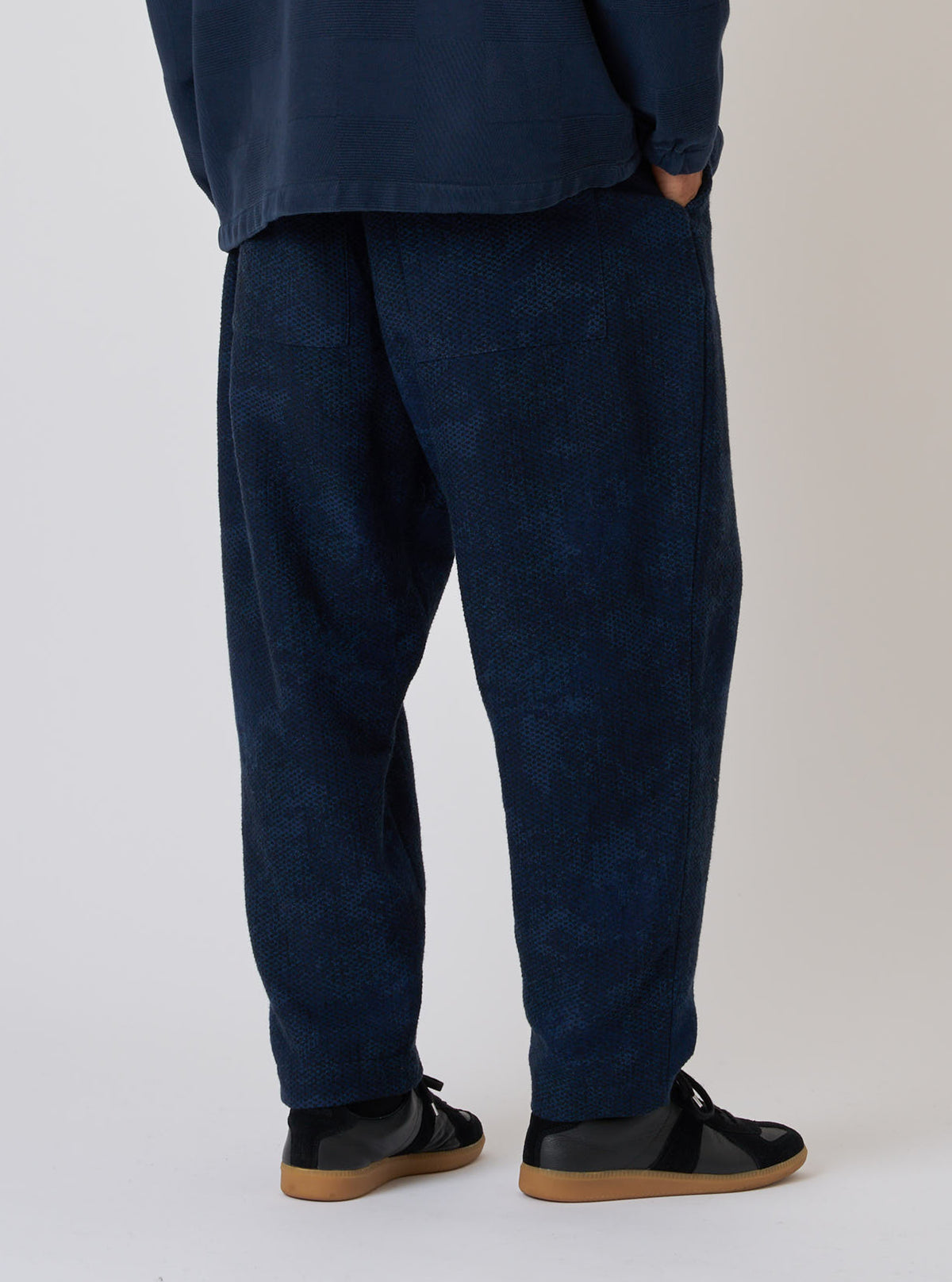 Back view of a model wearing the Black/Indigo Denim Camo Braga Pant. The pants are loose-fitting and paired with black shoes, set against a plain background.