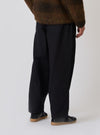 Back view of a model wearing the Black Organic Canvas Dutch Pant. The pants are paired with a brown sweater and black sneakers. The background is a plain white studio backdrop.