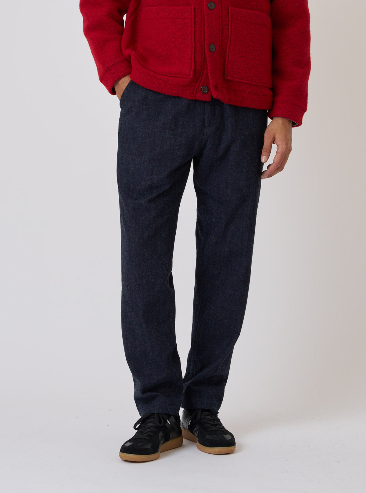 Studio shot of a model wearing Indigo Brushed Denim Military Chino, paired with a red jacket and black sneakers. The background is a clean, light color.