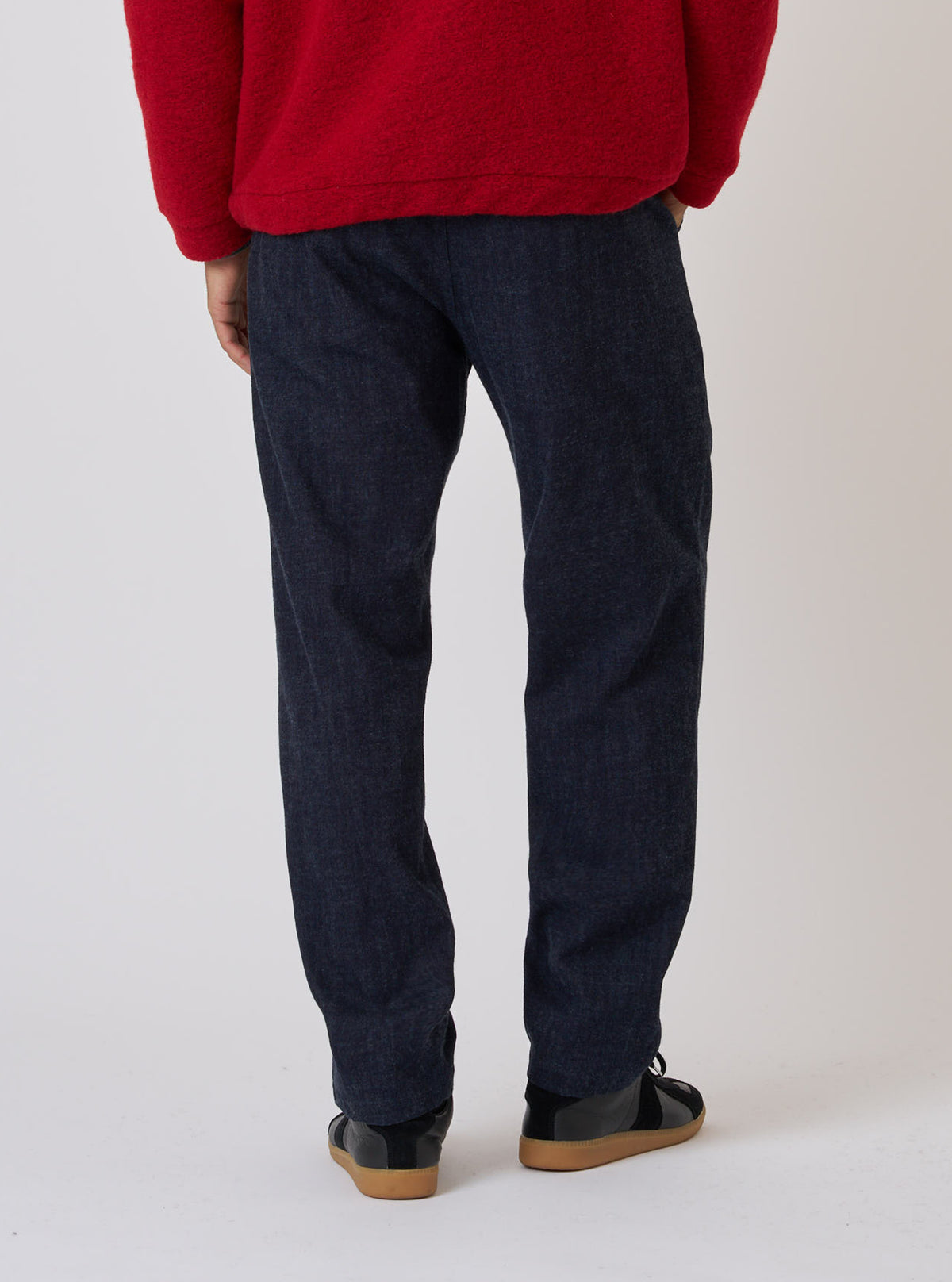Back view of a model wearing Indigo Brushed Denim Military Chino, paired with a red sweater and black shoes. Shot against a plain white backdrop.