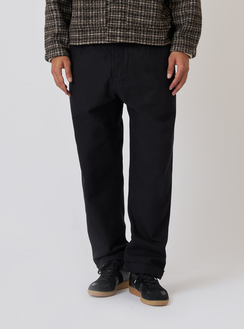 A model stands against a white backdrop wearing the Black Organic Canvas Super Chino. The chinos are paired with black sneakers and a patterned jacket.