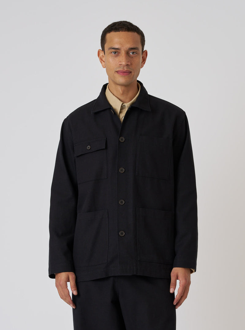 A model wears the Black Organic Canvas Dockside Overshirt. The overshirt is black canvas with brown buttons. Shot in front of a white background.