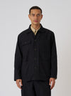 A model wears the Black Organic Canvas Dockside Overshirt. The overshirt is black canvas with brown buttons. Shot in front of a white background.