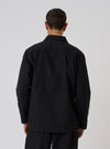 Back view of a model wearing a Black Organic Canvas Dockside Overshirt. The overshirt is made of black canvas. The background is a plain white studio backdrop.