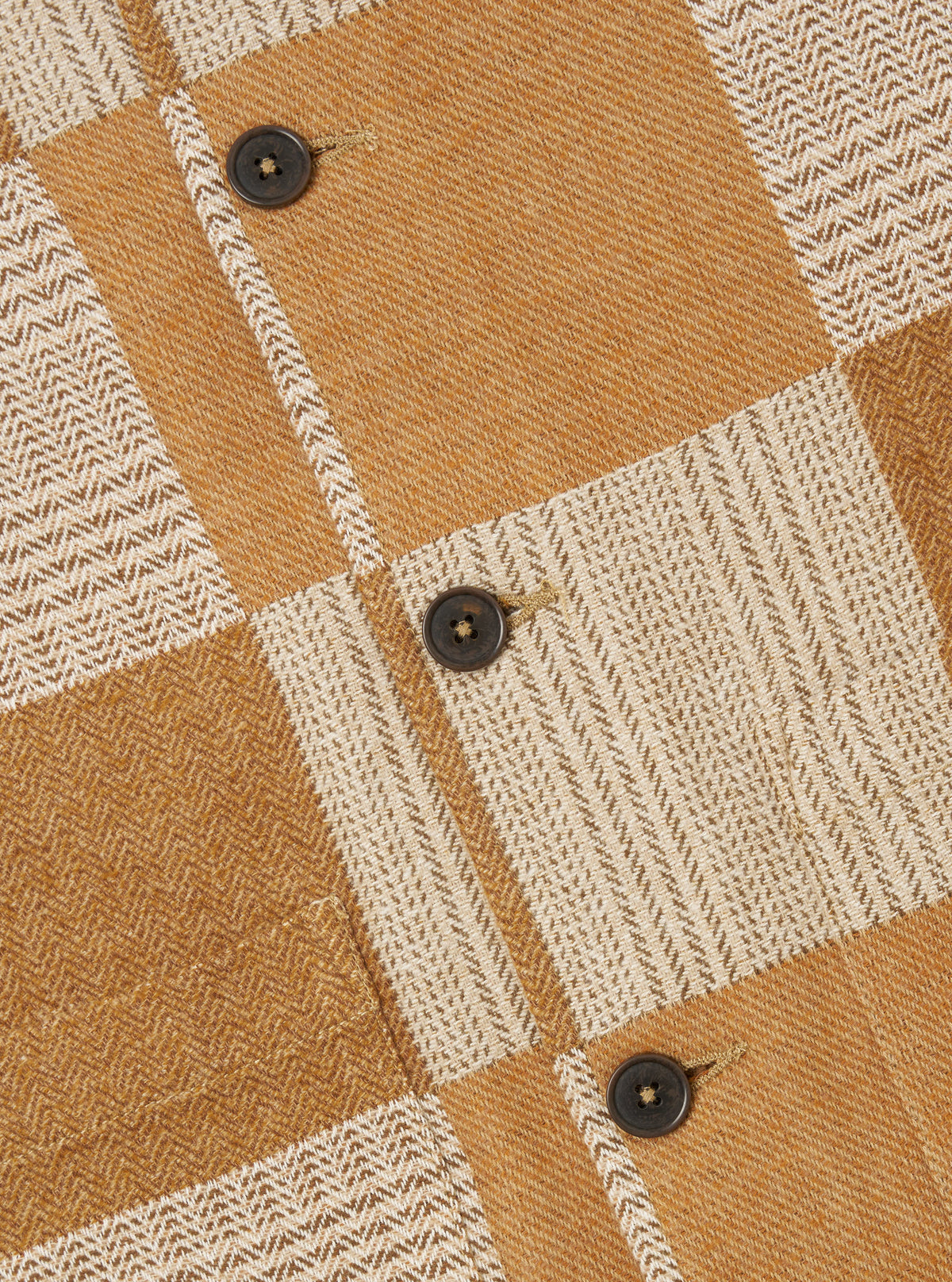 Close-up of the Sand Japanese Patchwork Easy Jacket. Features a tan and cream patchwork design with dark brown buttons. The jacket is laid flat on a neutral surface.
