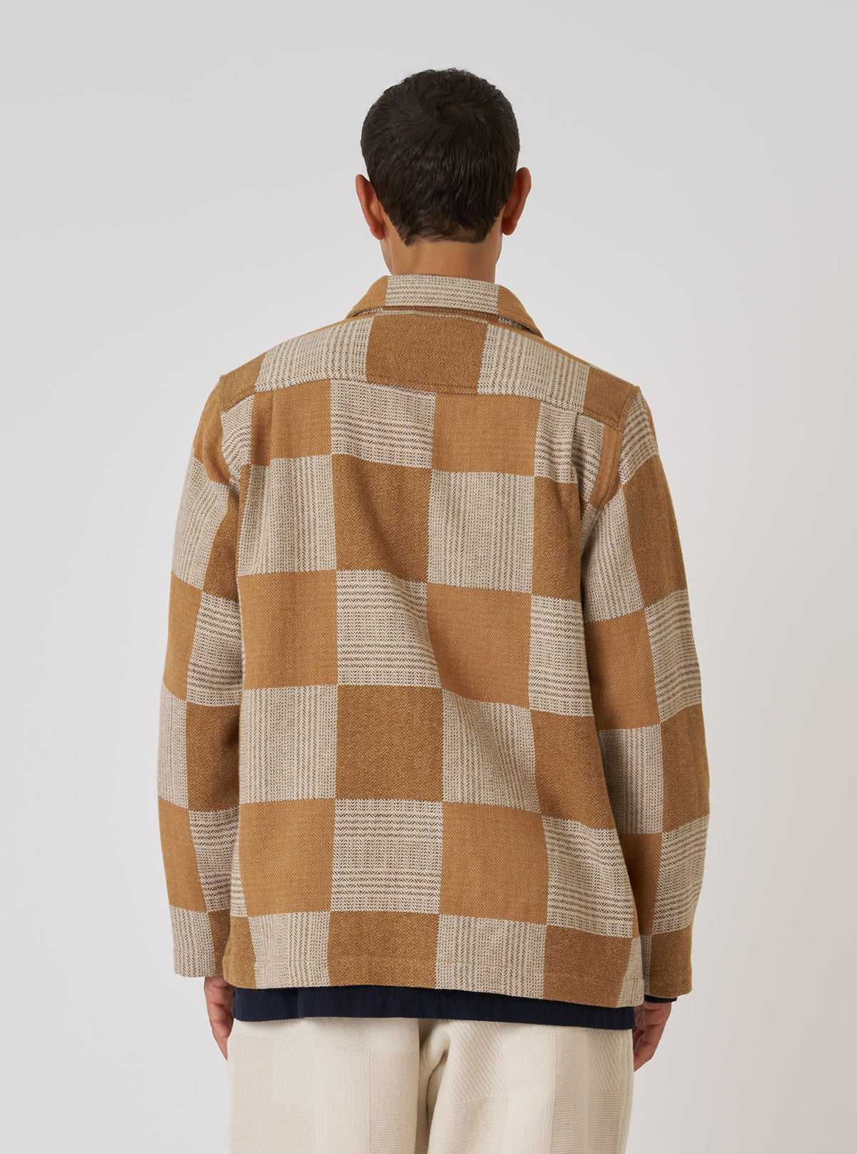 Back view of a model wearing the Sand Japanese Patchwork Easy Jacket. The jacket features a brown and beige checkerboard pattern. Shot against a white background.