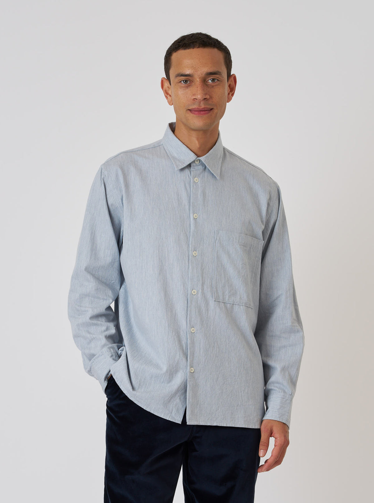 A man poses in front of a white backdrop, wearing a Sky Blue Brushed Organic Cotton Square Pocket Shirt. The shirt is buttoned and has a relaxed fit.