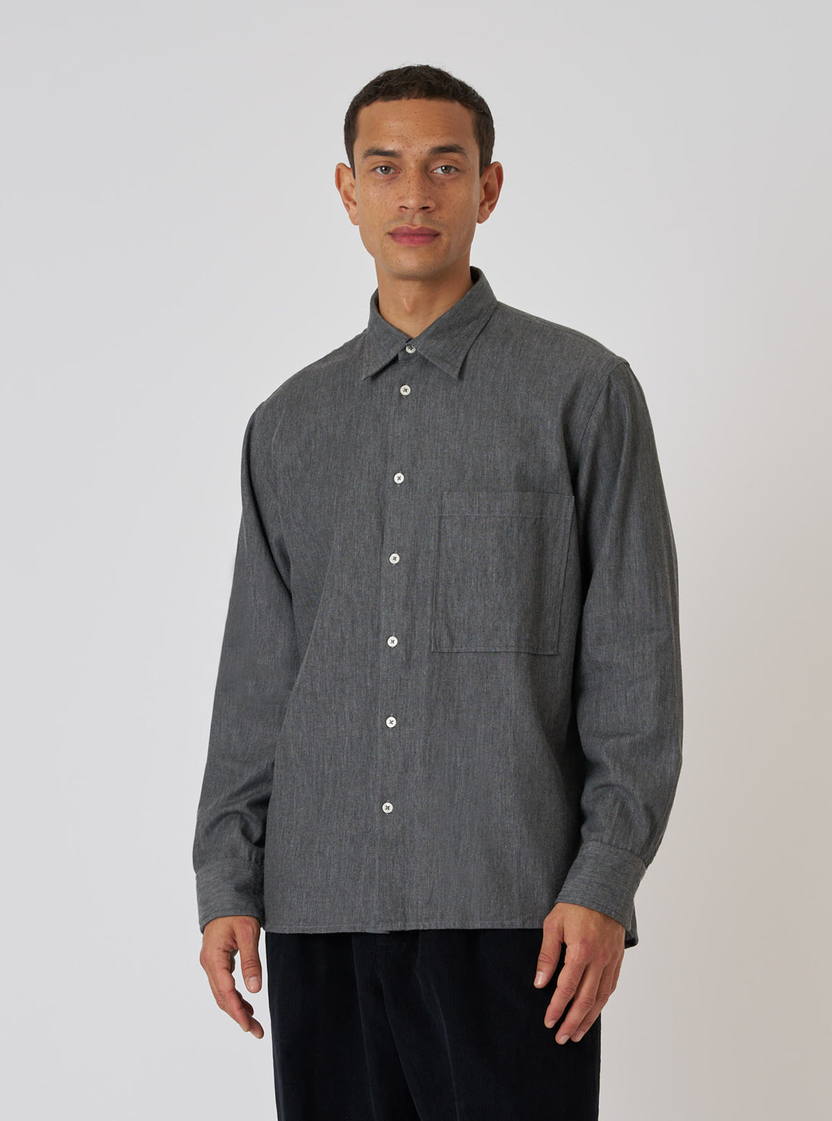 A model poses in a Charcoal Brushed Organic Cotton Square Pocket Shirt against a white backdrop. The shirt is a charcoal color and has a square pocket.