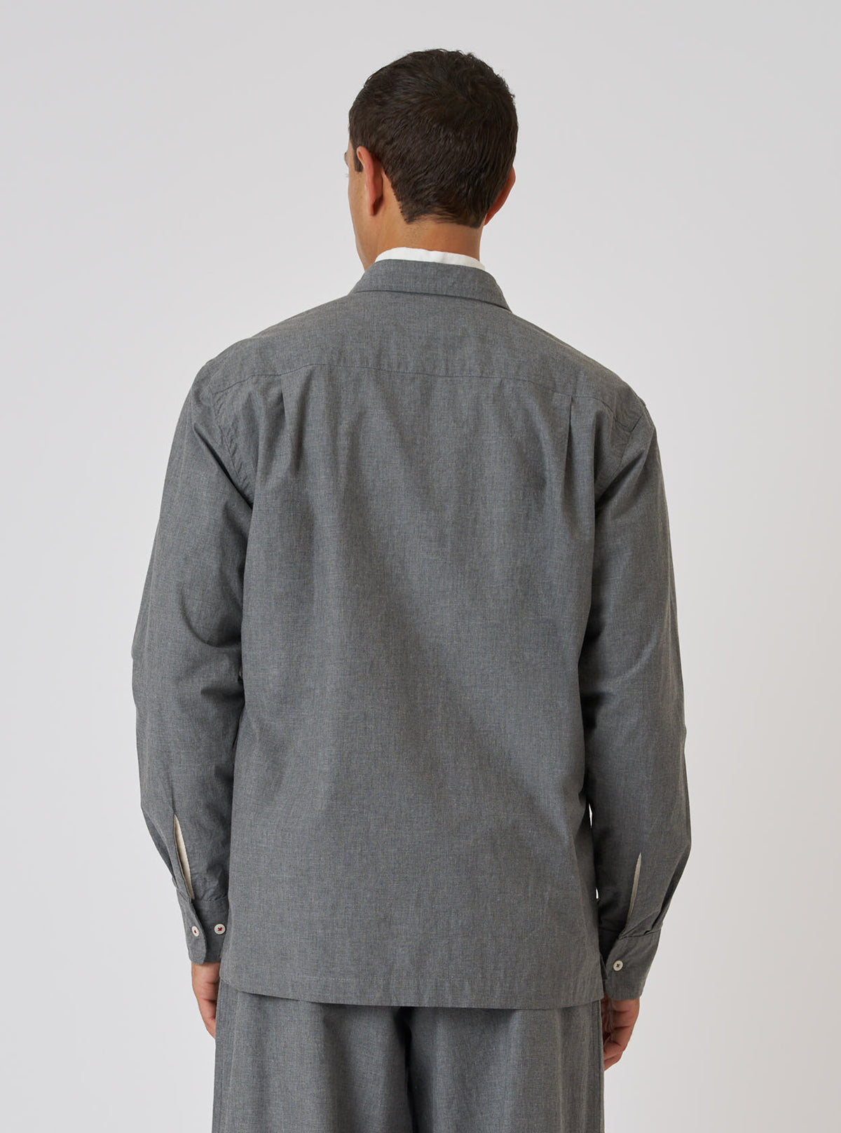 Back view of a model wearing the Charcoal Organic Chambray Lucky Shirt. The shirt is a relaxed fit and made of a textured charcoal fabric. Simple white studio background.