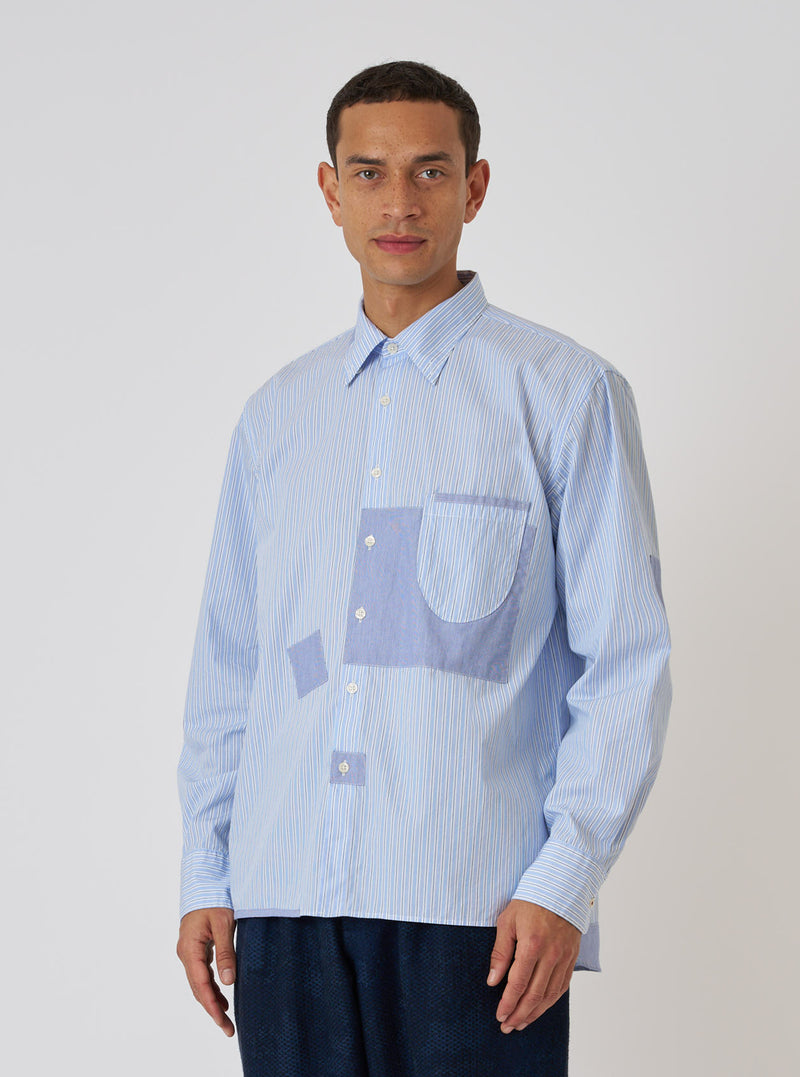 A model poses in front of a white background wearing a Blue Office Stripe Patched Lazy Day Shirt. The shirt is blue and white striped with light blue patches.