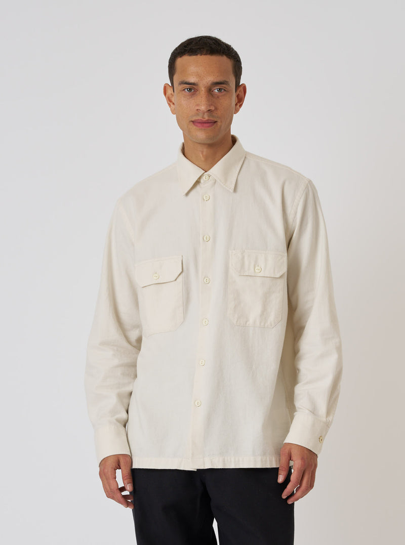 A man poses in the Ecru Sid Flannel CPO Shirt against a white backdrop. The shirt is a light, natural color with a relaxed fit. He's wearing dark pants.