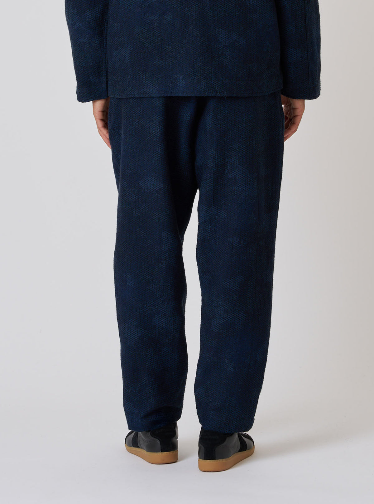 Back view of a model wearing Black/Indigo Denim Camo Pleated Track Pant on a white background. The denim pants have a loose fit and subtle camo pattern.