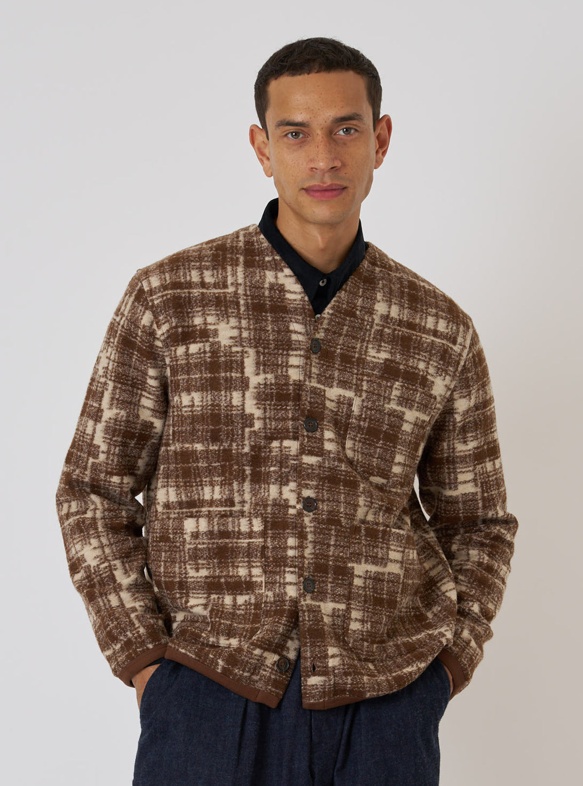 A model poses against a white backdrop wearing the Sand Patch Check Fleece Cardigan. The cardigan features a brown and beige check pattern and a relaxed fit.