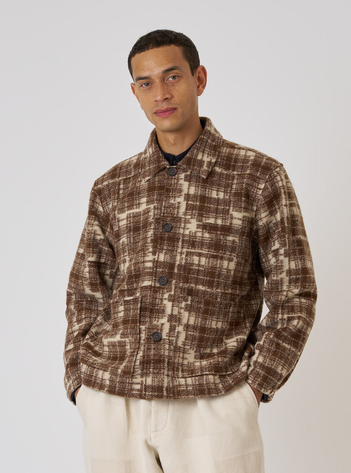 A man poses in front of a white background, wearing the Sand Patch Check Fleece Rams Jacket. The jacket is brown and beige with a check pattern.