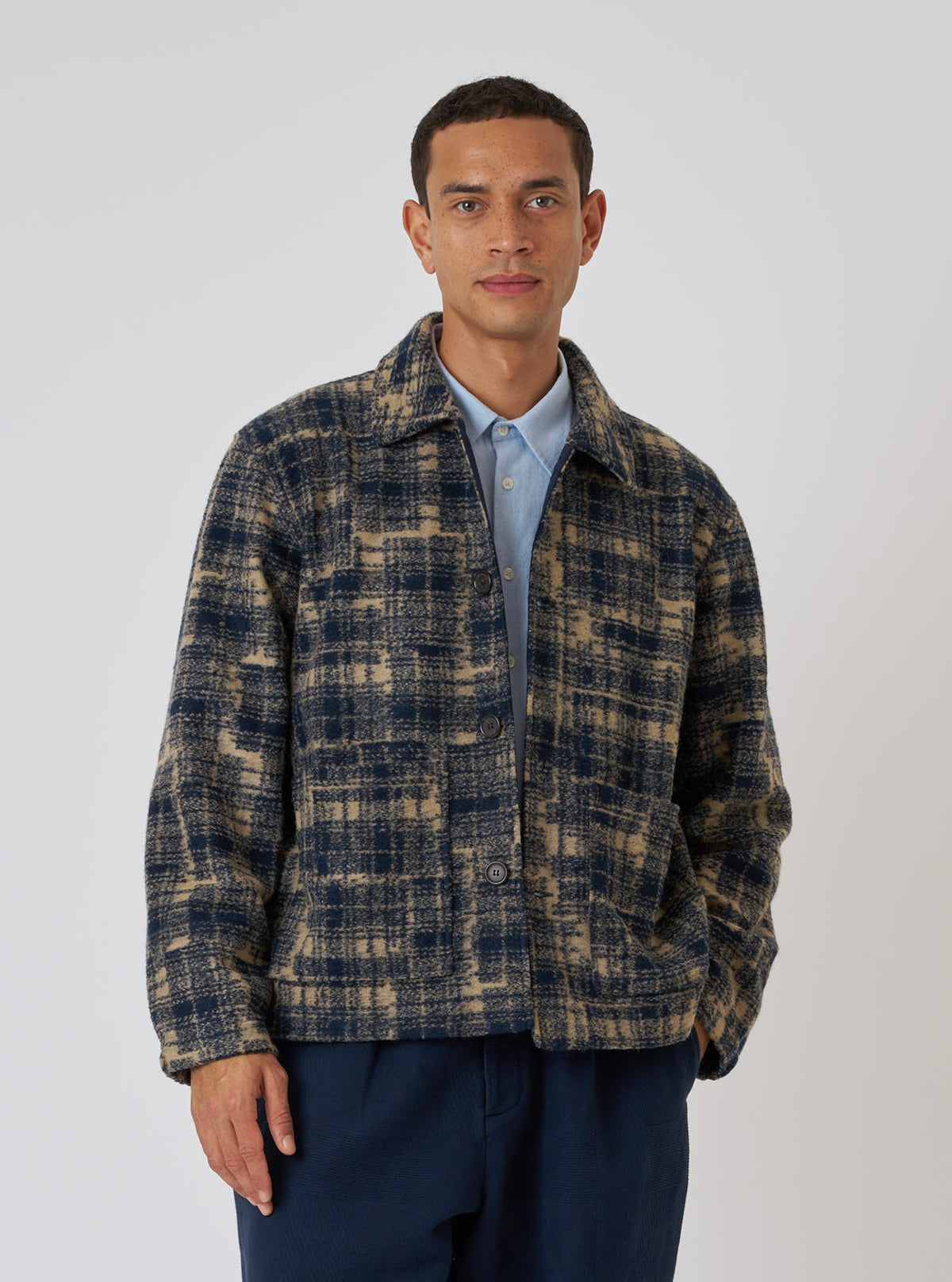 A man poses in front of a white background wearing the Navy Patch Check Fleece Rams Jacket. The jacket is a blue and tan plaid.