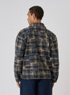 A man stands against a white backdrop, modeling the Navy Patch Check Fleece Rams Jacket. The jacket features a navy and tan check pattern.