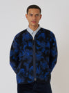 A man stands against a white backdrop, wearing a Blue Flower Fleece Zip Liner Jacket. The jacket features a blue and black floral pattern and a zip-up front.