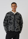 A model poses in a Charcoal Flower Fleece Zip Liner Jacket against a white backdrop. The jacket features a black and gray floral pattern and a zip-up front.