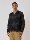 A man poses in front of a white background wearing a Navy Deca Check Cardigan. The cardigan is navy and brown with a button-up front and pockets.