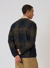 A man in a Navy Deca Check Cardigan poses against a white background. The cardigan features a navy and brown check pattern. He wears tan pants and a collared shirt.