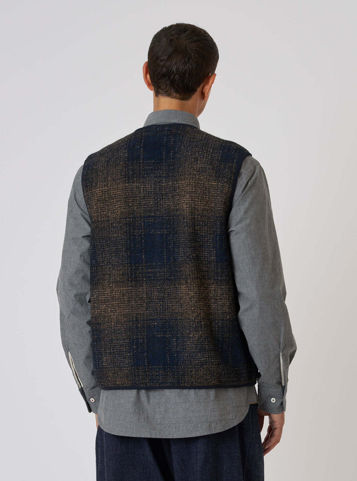Back view of a model wearing a Navy Deca Check Zip Gilet. The gilet features a navy and brown check pattern. The model is wearing a grey shirt. Simple white studio background.