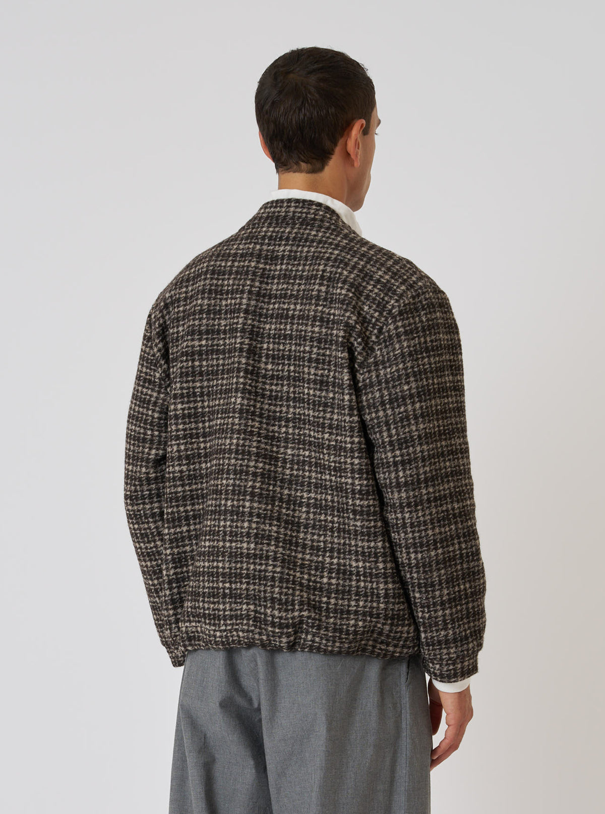 A man stands against a white backdrop, modeling the Brown Jacquard Knit Advance Cardigan. The cardigan features a brown and beige pattern. He wears gray pants.