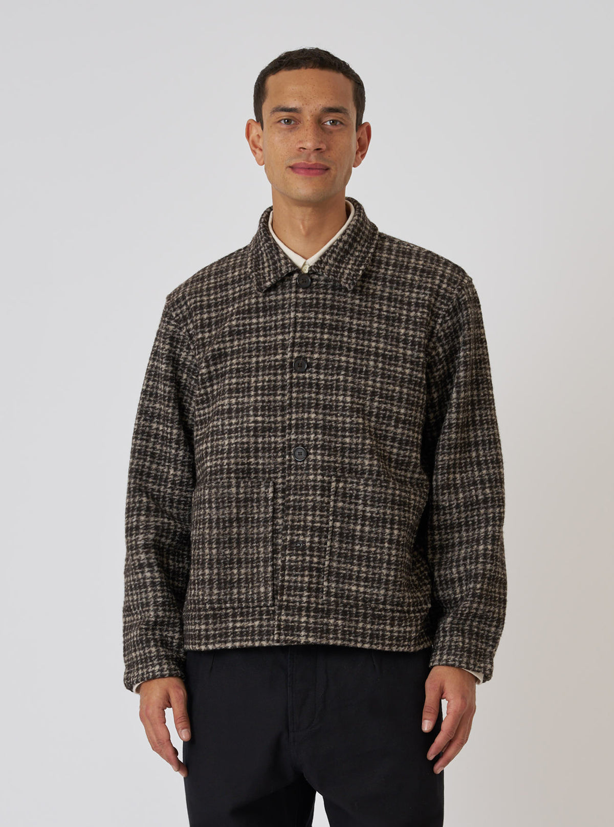 A model poses in a Brown Jacquard Knit Rams Jacket against a white backdrop. The jacket features a brown and beige pattern, button closure, and a relaxed fit.