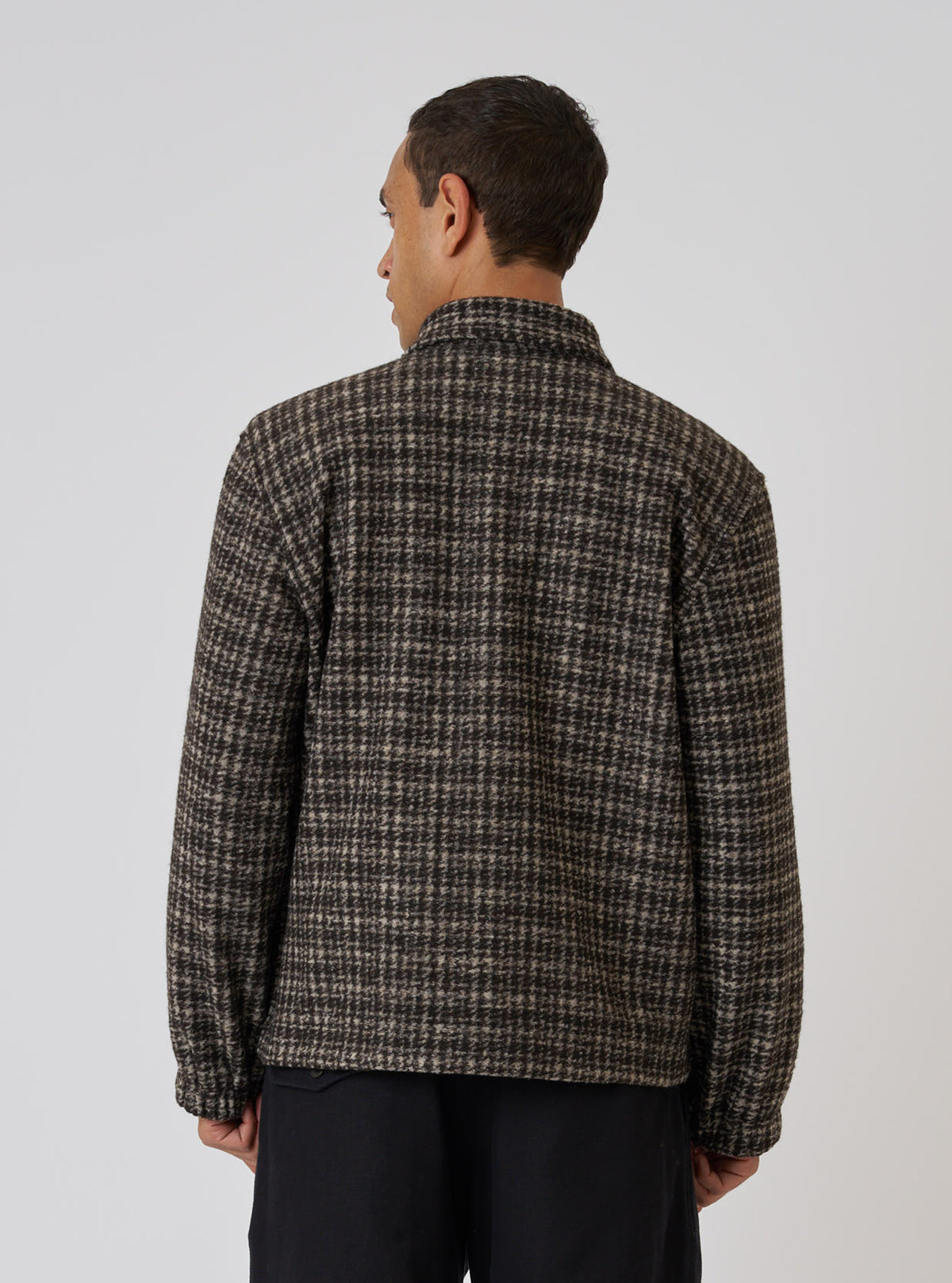 Back view of a model wearing a Brown Jacquard Knit Rams Jacket. The jacket has a brown and beige grid pattern. Shot against a plain white background.