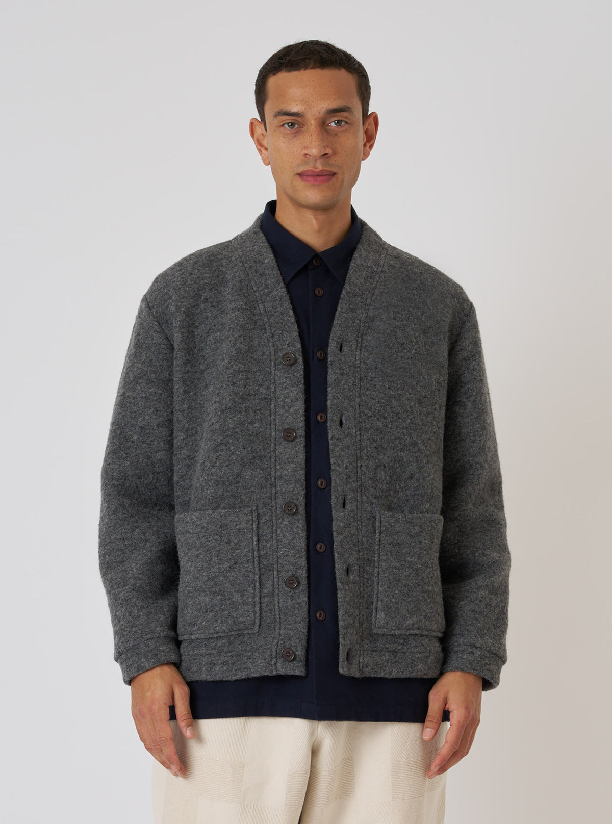 A model wears a Grey Marl Wool Fleece Advance Cardigan in front of a white background. The cardigan is buttoned and has two pockets.