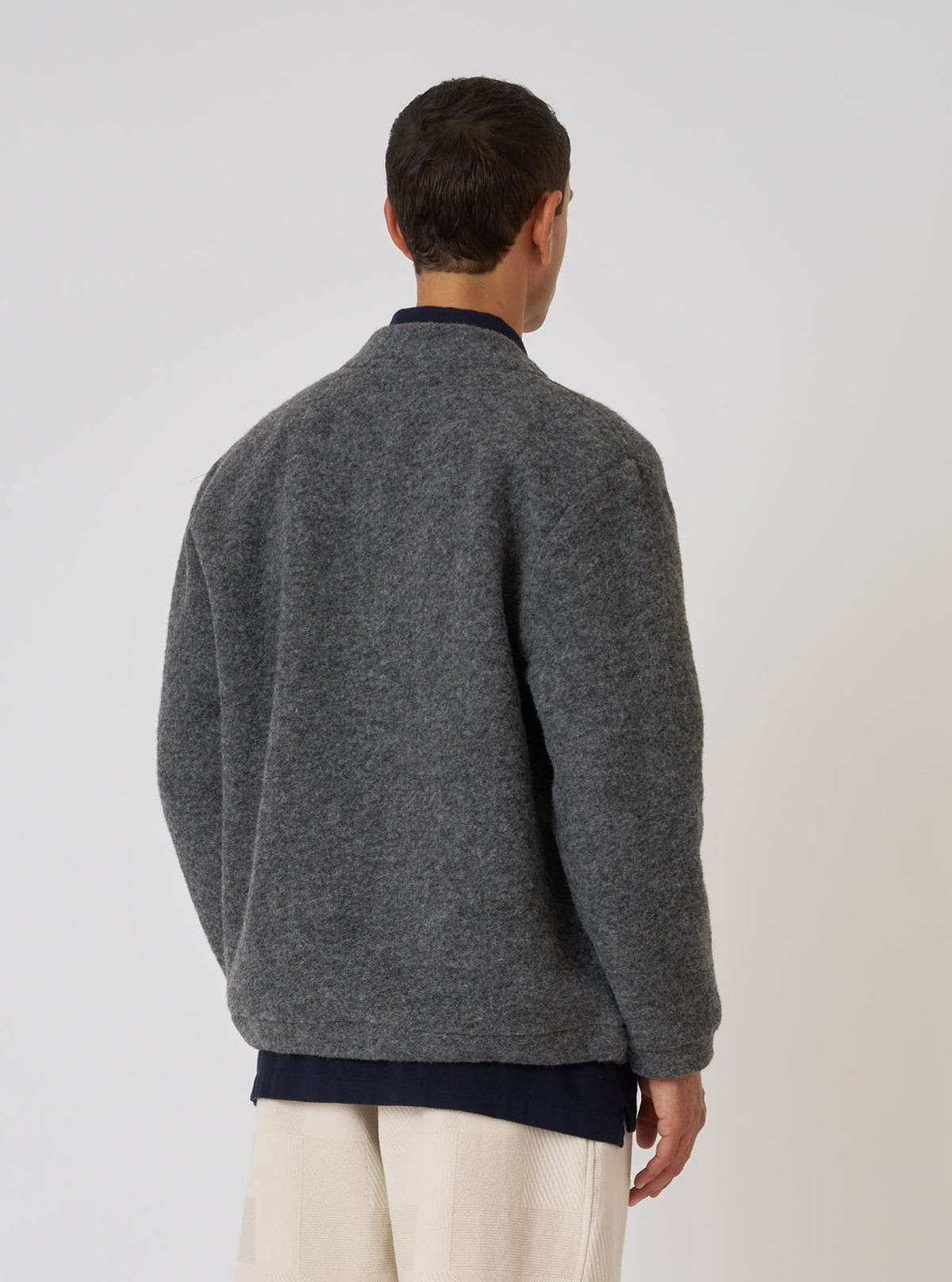 Back view of a model wearing the Grey Marl Wool Fleece Advance Cardigan. The fleece is layered over a navy shirt and paired with cream pants. Shot against a plain white backdrop.