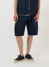 A male model is wearing the Navy Paper Touch Cotton Vacation Short against a plain white background. The image shows the shorts from the waist down, highlighting the crisp, navy blue fabric, side pockets, and a relaxed fit. The model is standing straight and is also wearing navy blue shoes.