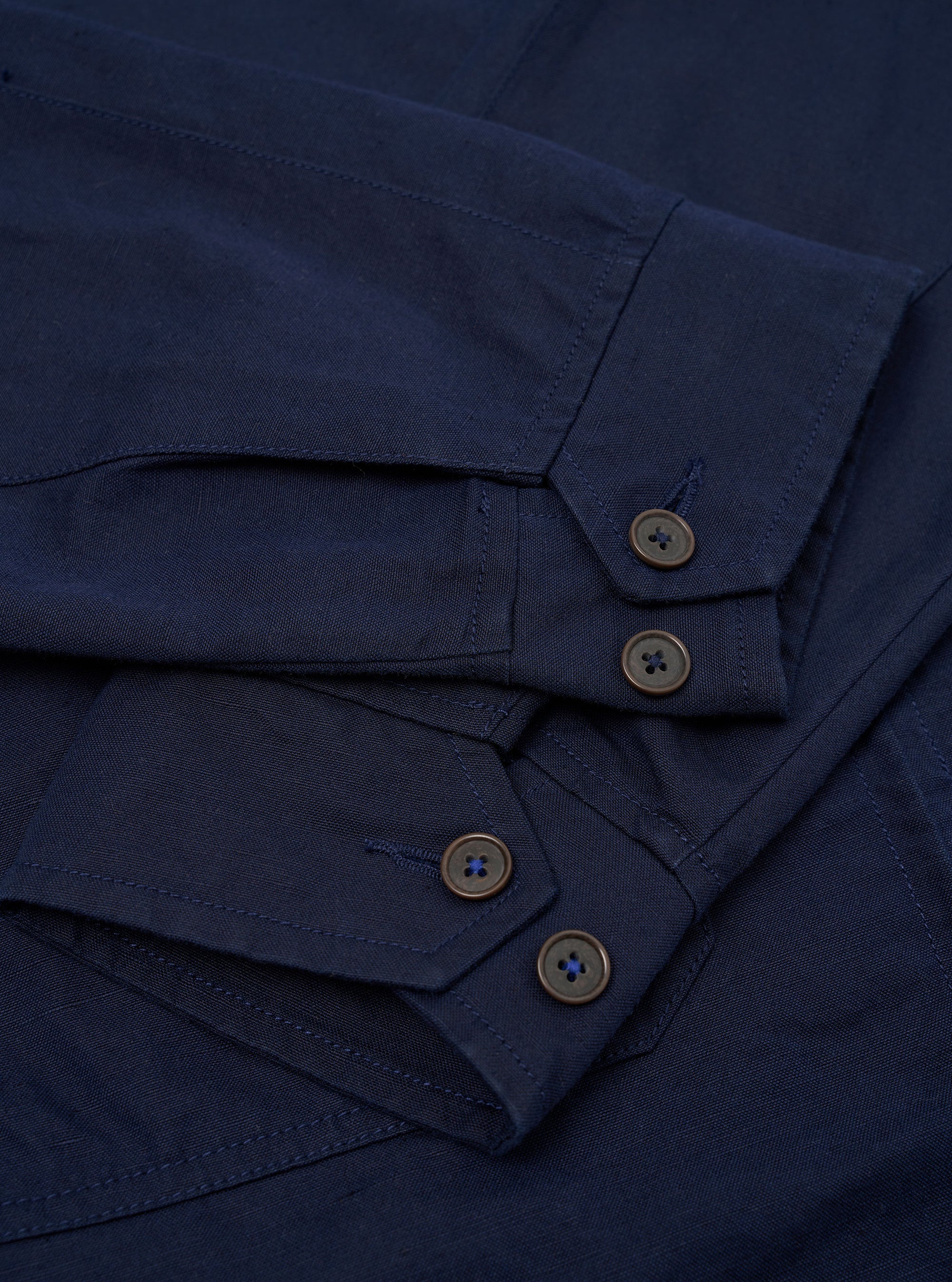The Navy Linen Slub Weave E130 Jacket is shown from the back, laid flat against a solid white background. The image highlights the jacket's simple, clean construction, featuring a straight hem and a classic collar.