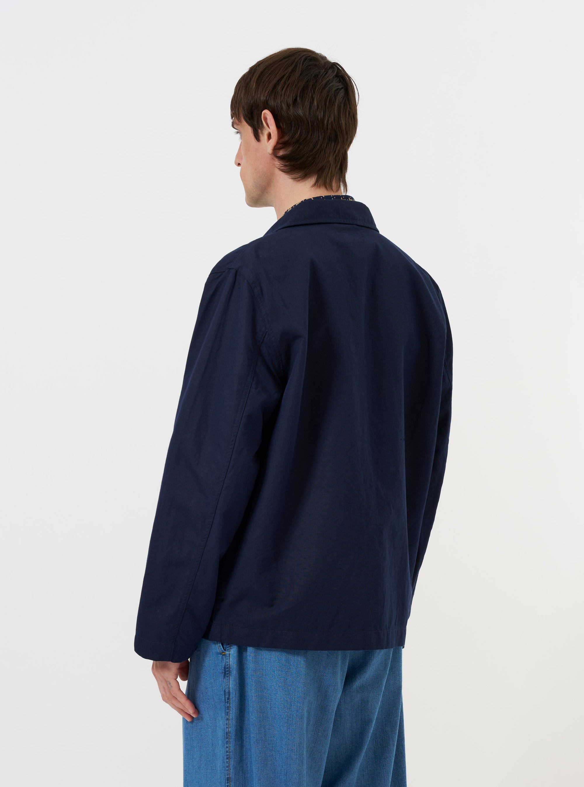 The back of the Navy Linen Slub Weave Franck Jacket is shown laid flat against a plain white background. The image highlights the textured navy blue fabric and the clean, simple construction of the jacket's rear, featuring a straight hem and the back of the classic collar.