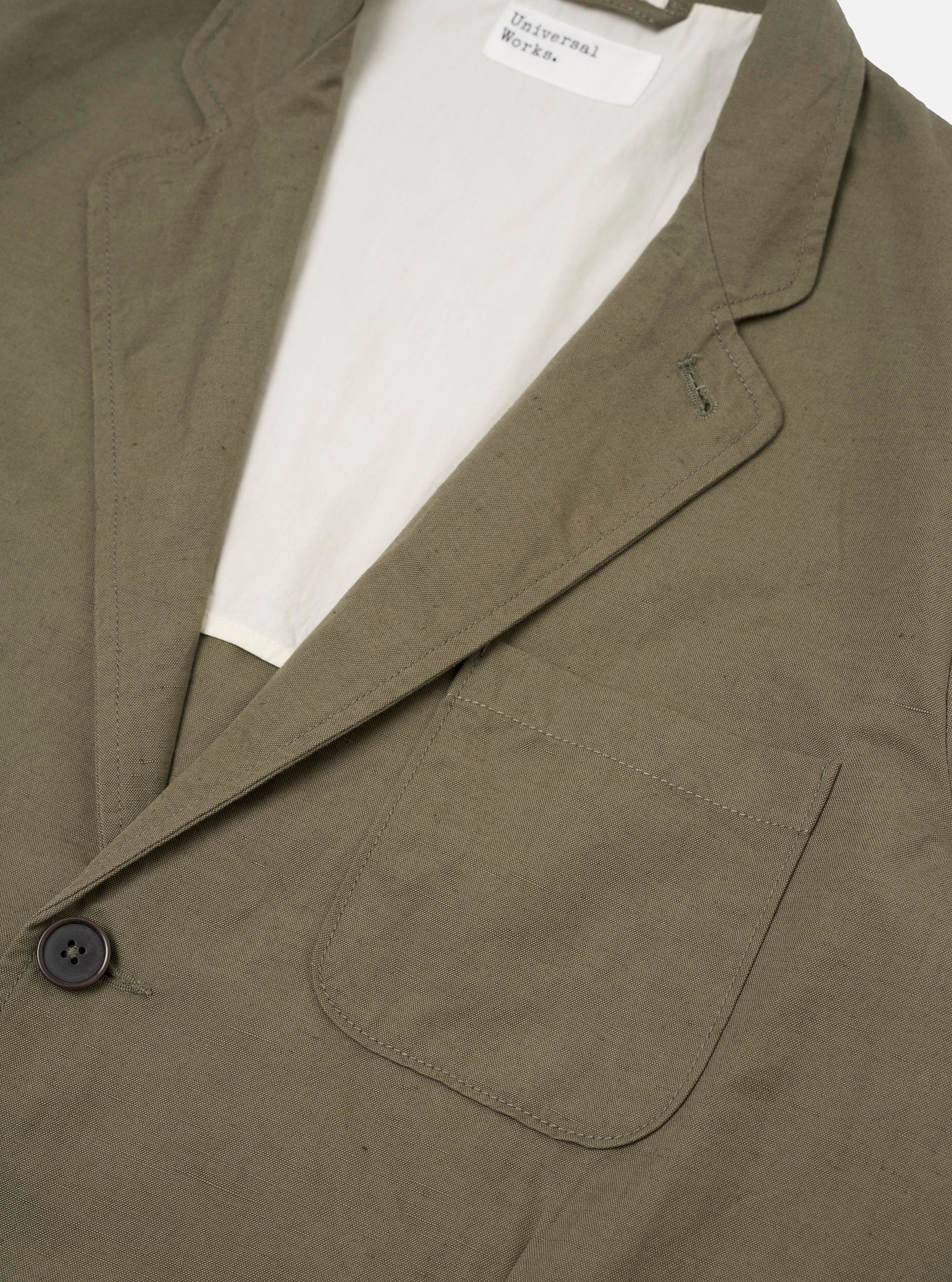 The Olive Linen Slub Weave Two Button Jacket is shown from the back, laid flat against a plain white background. The image highlights the structured shoulders, vertical rear seams, and a single central vent at the hem. The olive green fabric features a distinct slubby texture.