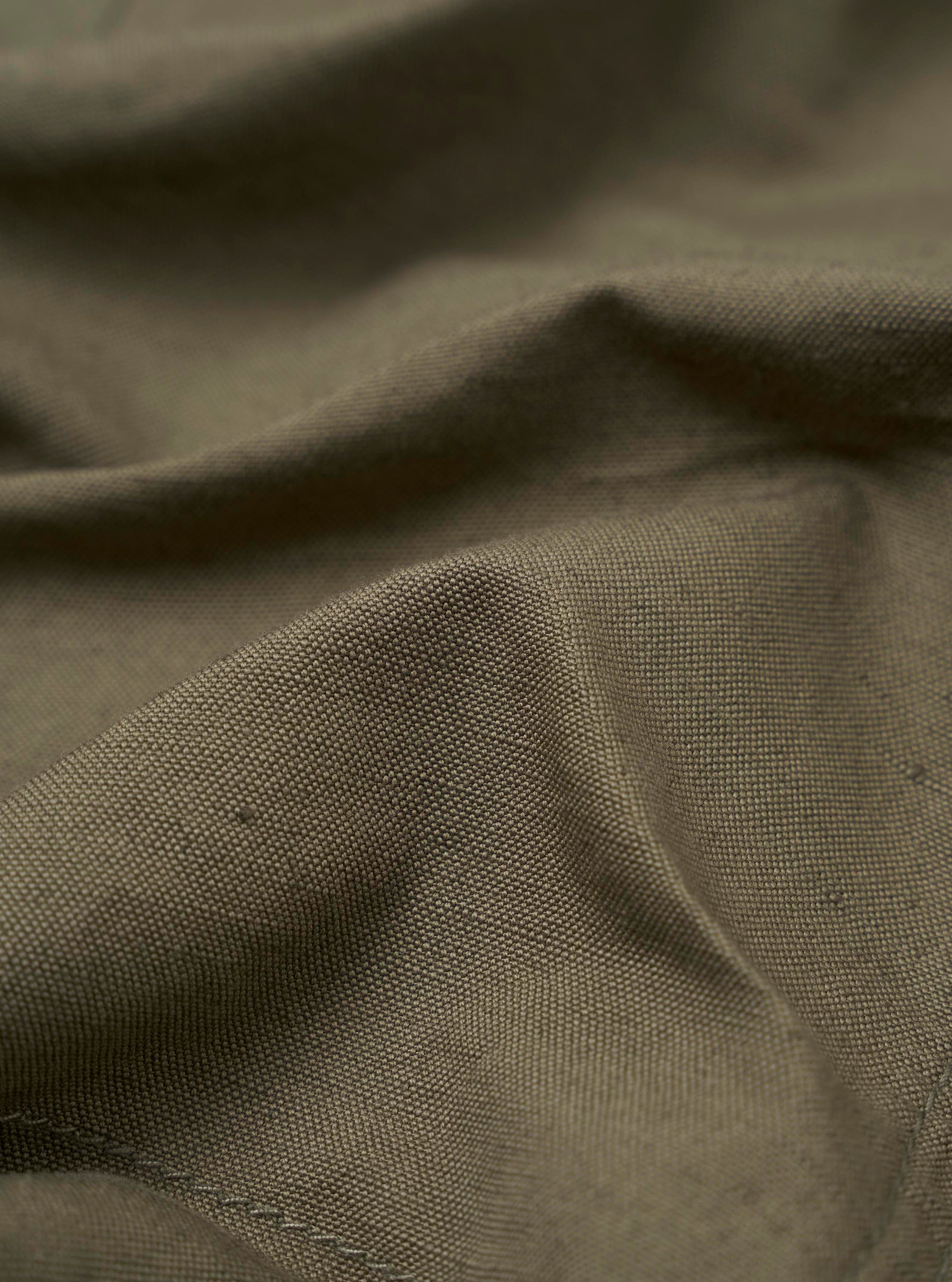 A close-up fabric swatch of the Olive Linen Slub Weave Bakers Jacket displays the detailed texture and irregular weave of the olive green linen-blend material. The fabric is shown as a flat, square sample with no model or mannequin present.