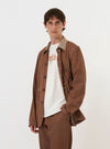A model is wearing the Brown Meco Denim OG Bakers Jacket against a plain white background. The brown denim chore jacket features a loose fit, a classic collar, and multiple front patch pockets with contrast stitching. The model is shown from the waist up, wearing the jacket over a light-colored shirt.
