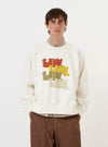 A model is wearing the Ecru Brush Back Sweat FM Raglan Sweatshirt against a plain white background. The image shows the sweatshirt from the front, highlighting the ribbed crew neck, raglan sleeves, and the soft, textured ecru cotton fabric. The model's hands are placed in the side pockets, showcasing the relaxed fit of the garment.