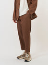 A male model is wearing a pair of Brown Meco Denim Hi Water Trousers, standing against a plain white background. The image prominently features the slim-fit, cropped leg of the trousers and the drawstring waistband. The model is also wearing dark shoes and white socks.