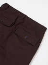 A pair of brown twill dizzy trousers is displayed from the back, laid flat against a solid white background. The image highlights the wide-leg cut and two large rear patch pockets.