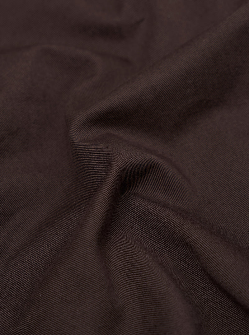 A close-up fabric swatch of the brown cotton twill material used for the Dizzy Trouser. The image captures the detailed diagonal weave and texture of the fabric.