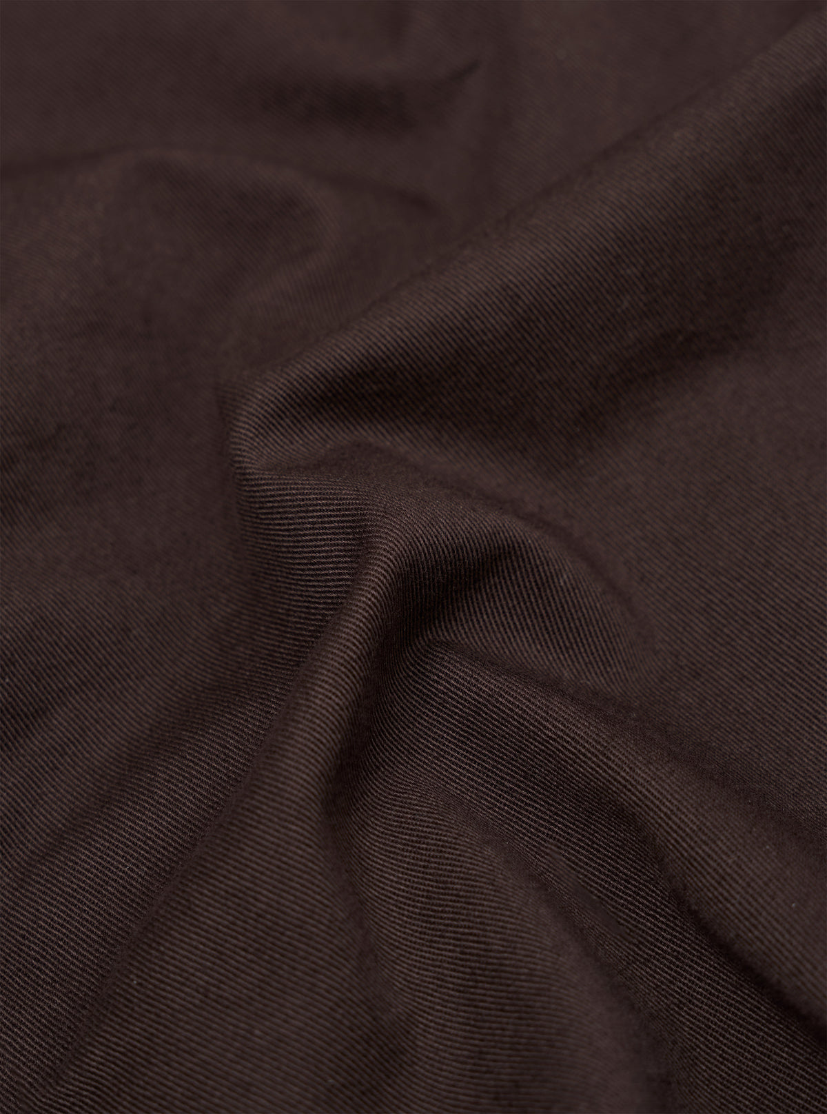 A close-up fabric swatch of the brown cotton twill material used for the Dizzy Trouser. The image captures the detailed diagonal weave and texture of the fabric.