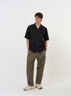 The Black Broadcloth Camp Shirt is shown laid flat against a solid white background. The shirt features a camp collar, a full button-down front, and short sleeves. A single patch pocket is visible on the left chest. The garment is solid black with a smooth, matte finish.