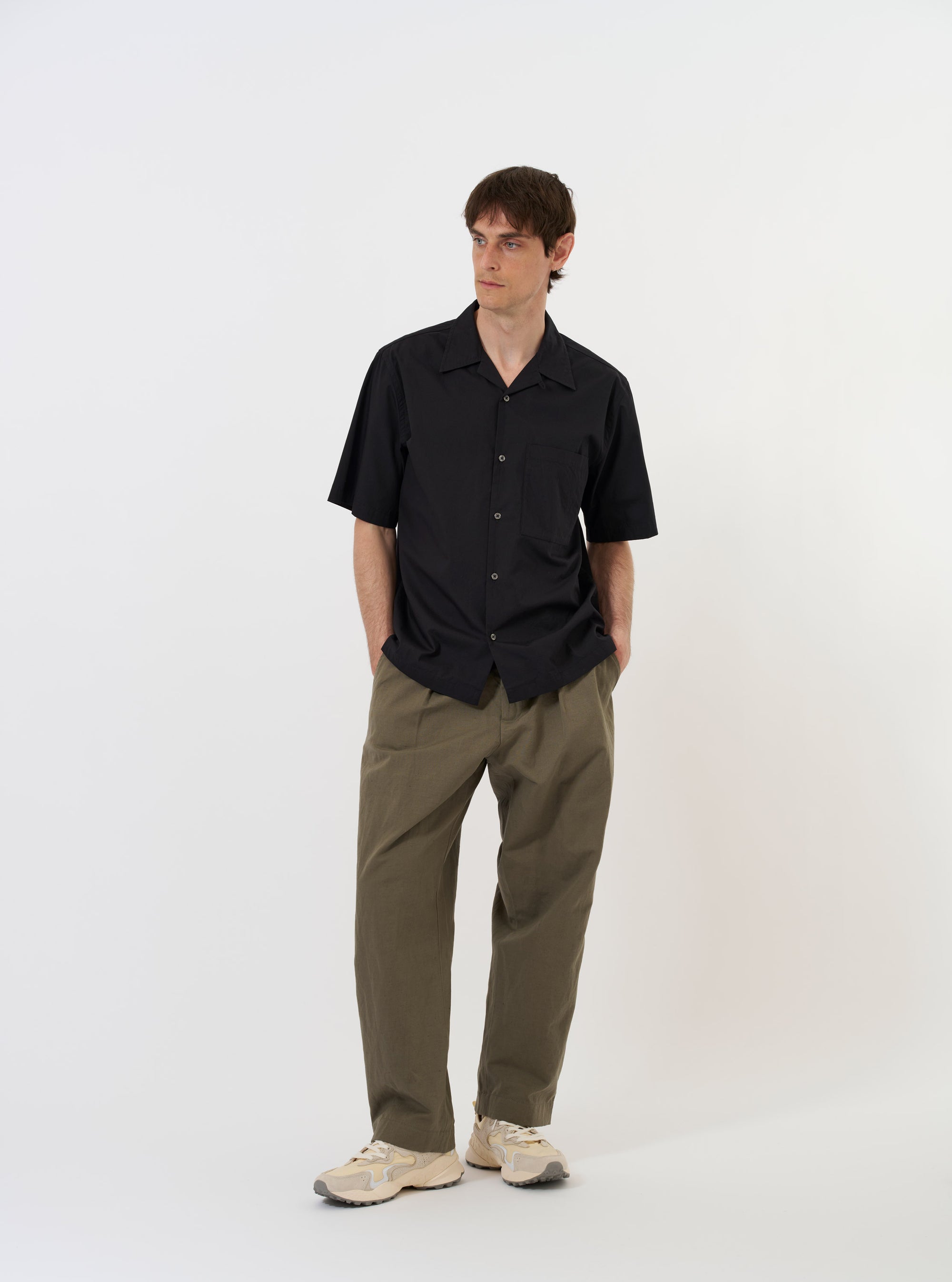 The Black Broadcloth Camp Shirt is shown laid flat against a solid white background. The shirt features a camp collar, a full button-down front, and short sleeves. A single patch pocket is visible on the left chest. The garment is solid black with a smooth, matte finish.