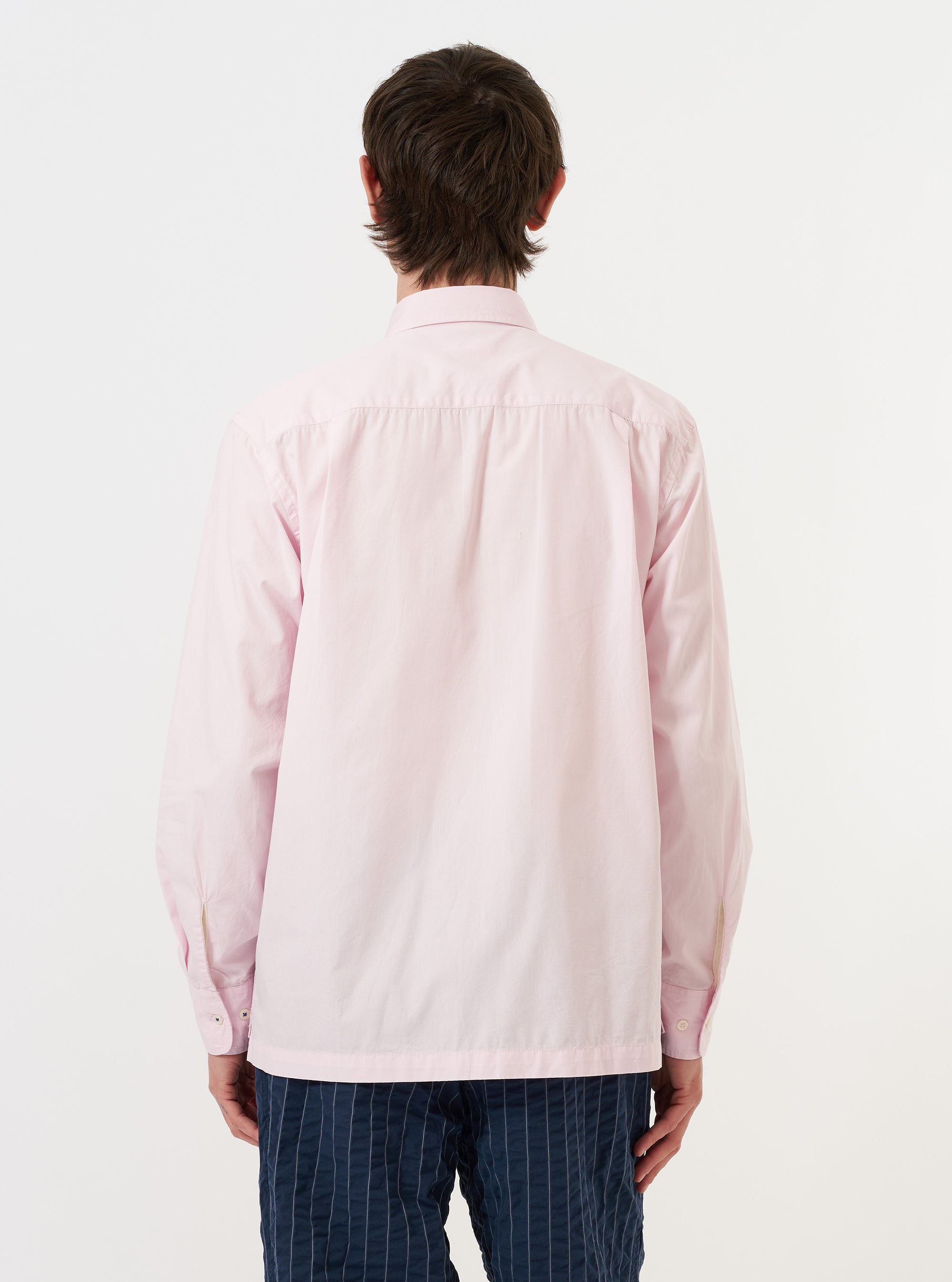 A model is wearing the Pale Pink Broadcloth Lucky Shirt against a plain white background. The shirt is shown from the back, highlighting the yoke, the hang loop, and the relaxed fit of the pale pink broadcloth fabric. The model is also wearing dark trousers.