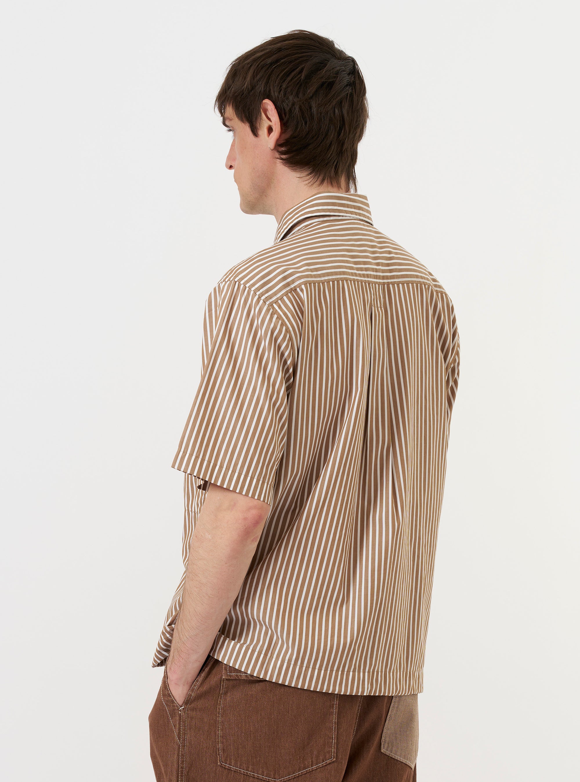 A model is wearing the Brown/White Cotton Stripe Z Tech Overshirt, seen from the back against a plain white background. The overshirt features a pattern of vertical brown and white stripes, a horizontal back yoke, and a classic pointed collar. The model is standing and has the garment paired with dark-colored trousers.