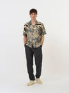 The Grey Baja Print Road Shirt is shown laid flat against a solid white background. This short-sleeve button-down features an all-over grey and white botanical print, a relaxed camp collar, and a single chest patch pocket on the left side. The garment has a straight hem and tonal buttons along the front.