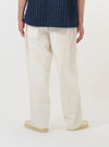 A model is wearing the Ecru Slub Drill Dutch Pant against a plain white background. The image provides a side-rear view of the trousers from the waist down, highlighting the loose, wide-leg fit and a single large patch pocket on the back. The model is also wearing navy blue shoes.