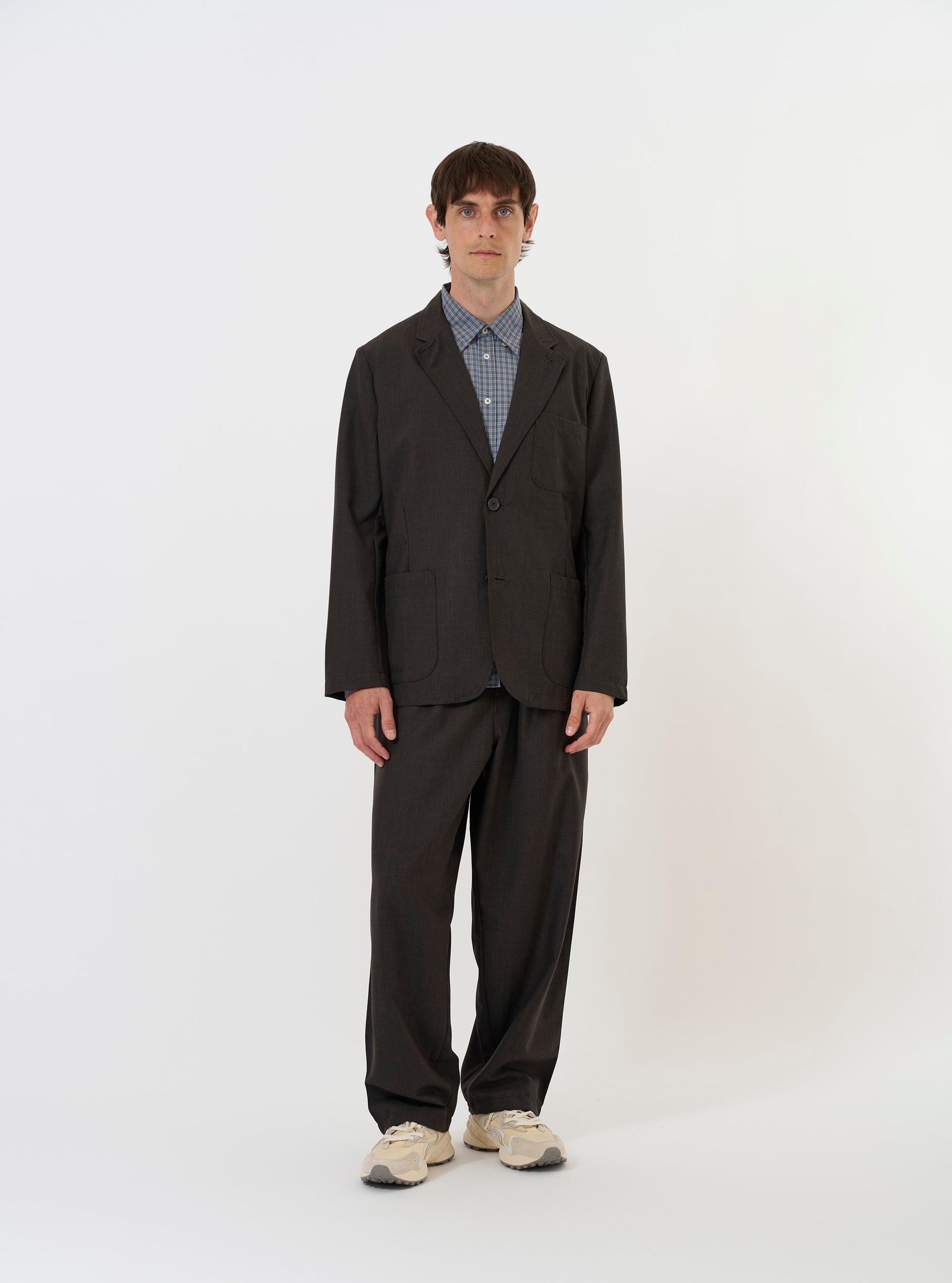 The Brown Marl Tropical Suiting Two Button Jacket is shown laid flat against a plain white background. The garment features a two-button front closure, a notched lapel, and three prominent patch pockets, including one on the chest and two at the waist. The jacket is constructed from a lightweight, textured brown marl fabric.